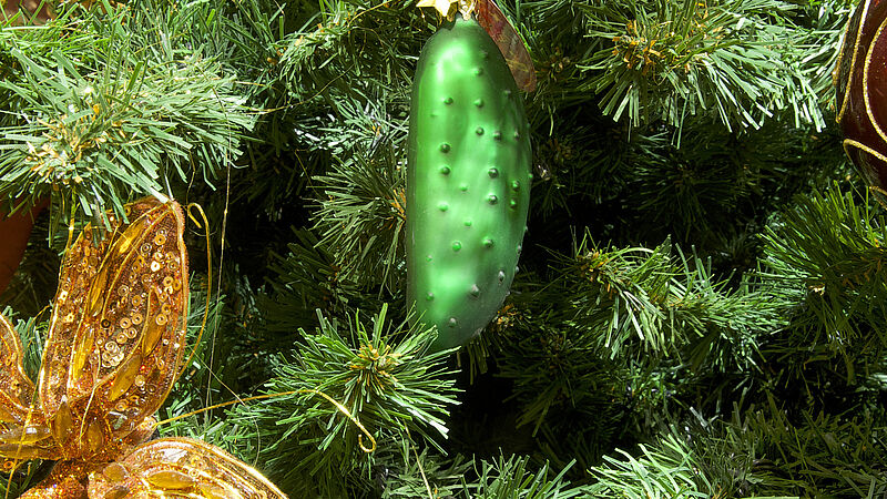 Eine grüne Weihnachtsgurke aus Glas hängt an einem geschmückten Baum.