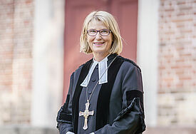 Pröpstin Frauke Eiben steht im Talar vor der Wand einer Kirche.