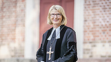 Pröpstin Frauke Eiben steht im Talar vor der Wand einer Kirche.