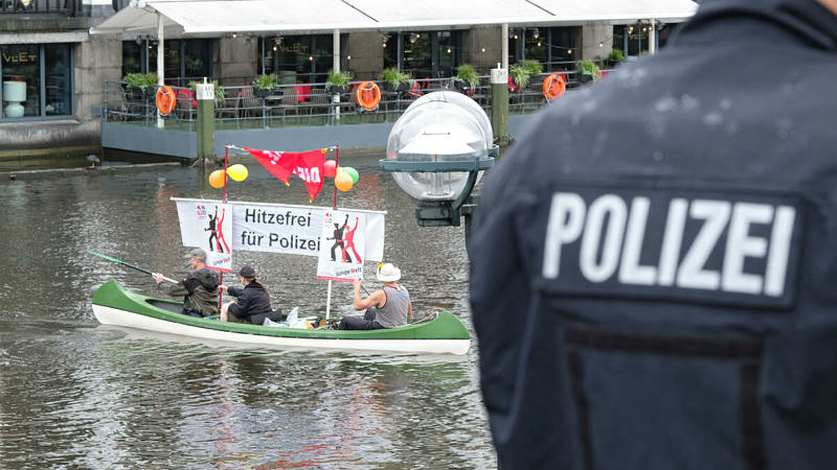 An der Hamburger Binnenalster sind am Sonntagmittag (02.07.17) bei stroemendem Regen Tausende Menschen zu einem bunten Protestzug durch die Stadt aufgebrochen (Foto: Demonstranten im Kanu auf der Kleinen Alster fordern Hitzefrei fuer Polizei - Ein Polizist steht am Ufer). Zuvor hatten 130 Boote auf dem Wasser mit Bannern und Transparenten gegen den bevorstehenden G20-Gipfel (7./8. Juli) protestiert. Die Veranstalter der "Protestwelle" sprachen von mehr als 18.000 Teilnehmern an Land, die Polizei zaehlte knapp 8.000. Die Demo ist die erste von derzeit etwa 30 angemeldeten Kundgebungen im Rahmen des Gipfels. 
