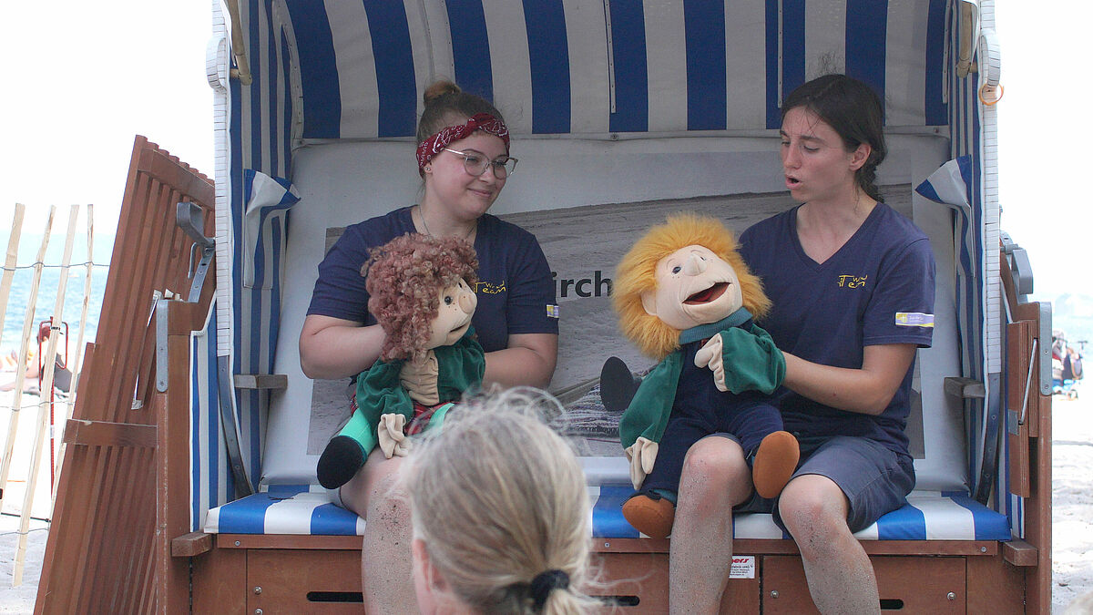 Angelina Thalau (links) und Kristin Schlegel erzählen mit Tom und Tina eine Geschichte im Strandkorb der Tourismuskirche.