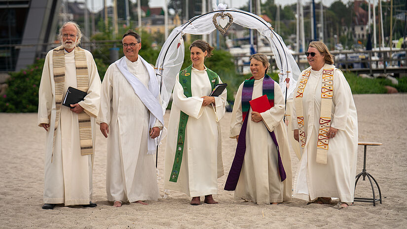 Vier Pastorinnen und Pastoren im Talar am Strand