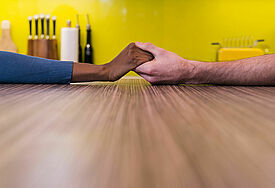 Zwei Menschen unterschiedlicher Hautfarben reichen sich die Hand auf einem Tisch