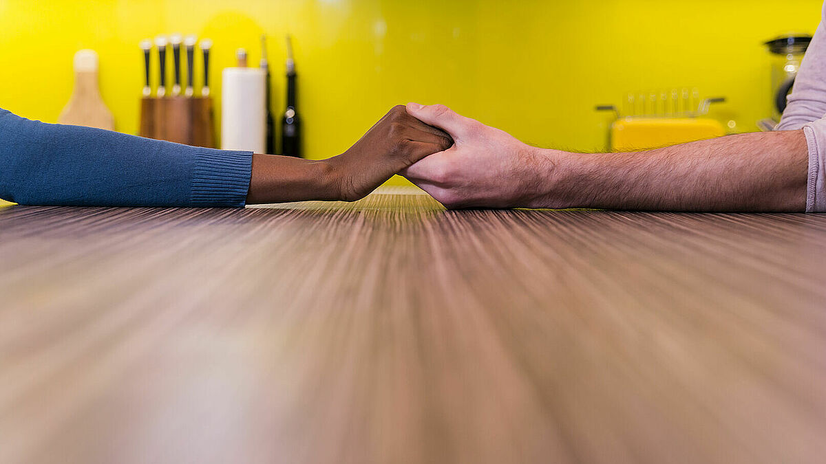 Zwei Menschen unterschiedlicher Hautfarben reichen sich die Hand auf einem Tisch