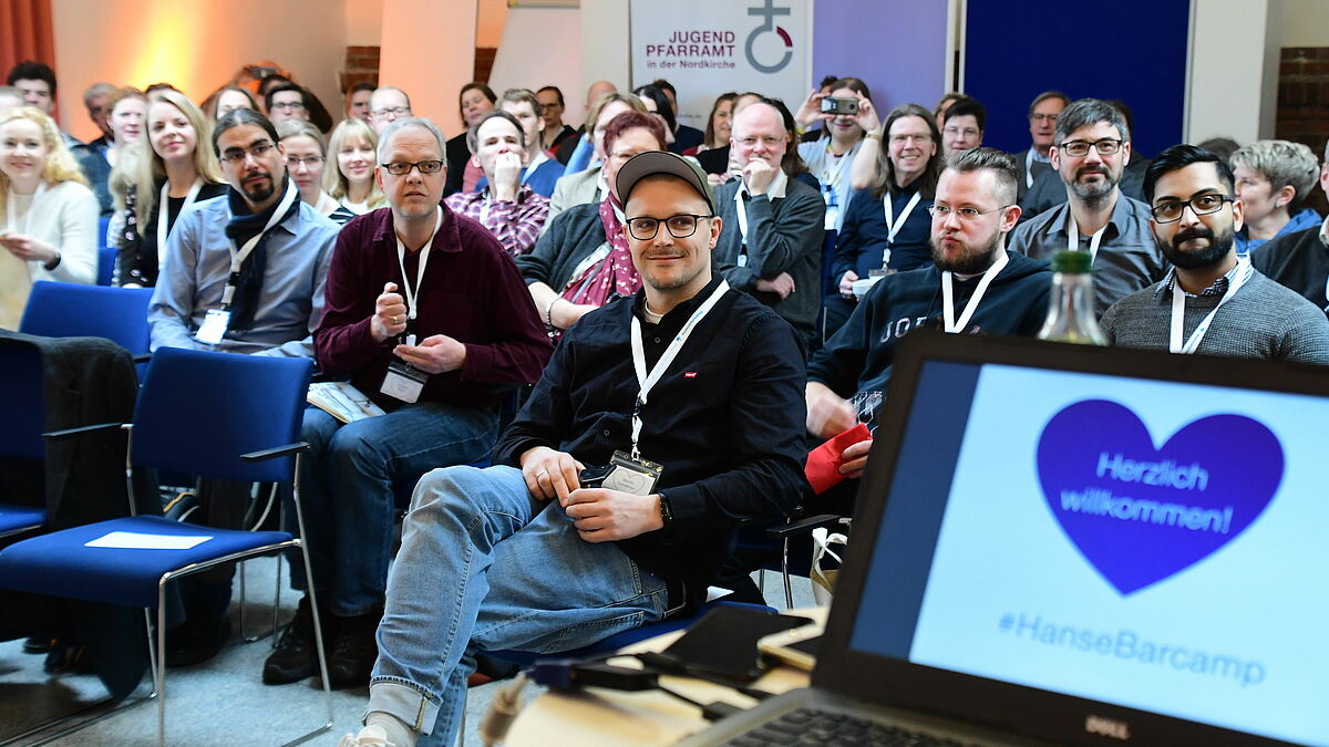 Kurz vor der Keynote von Martin Fehrensen (Mitte, erste Reihe) werden die Teilnehmerinnen und Teilnehmer des Hansebarcamps begrüßt.