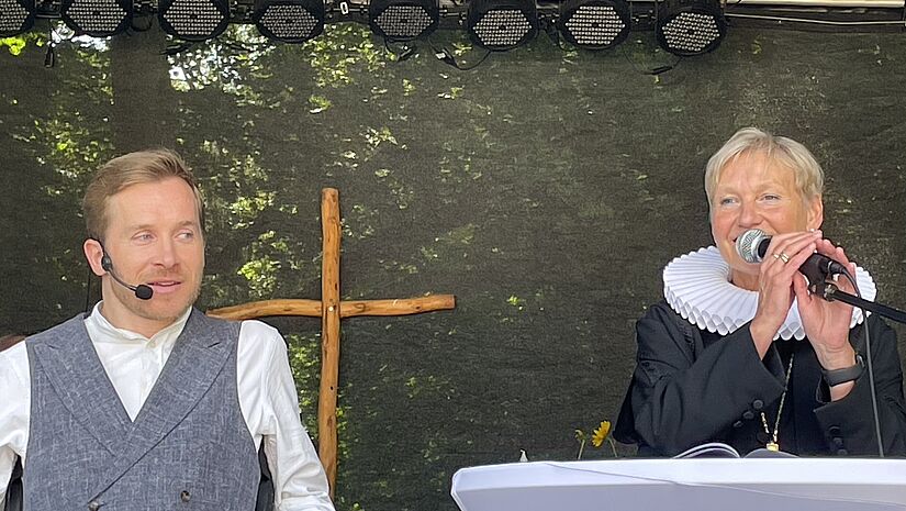 Schauspieler Samuel Koch und Bischöfin Kirsten Fehrs stehen auf der Open-Air-Bühne bei einer gemeinsamen Bibelarbeit