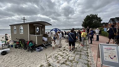 Menschen am Strand warten vor einem Bauwagen. 