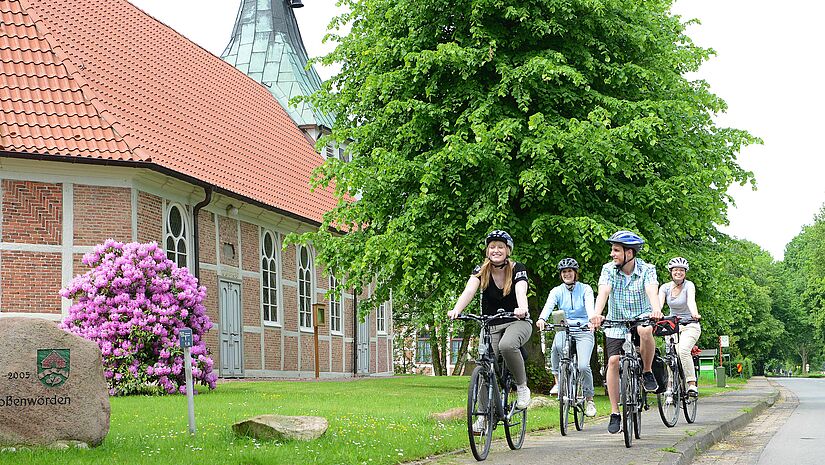 Eine Gruppe Fahrradfahrer fährt vorbei an einer Fachwerkkirche
