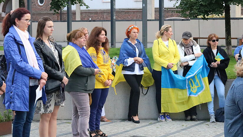 Frauen stehen im Halbkreis und beten, viele tragen blau-gelbe Kleidung oder Fahnen in den Farben der Ukraine.