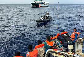 Menschen in Seenot im Schlauchboot, im Hintergrund ein großes Rettungsschiff
