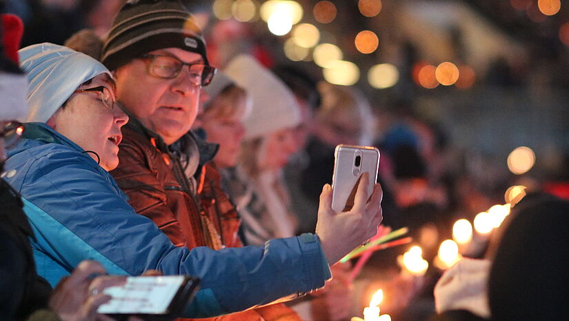 Zusammengerückt singt es sich noch schöner. Zwei Menschen schauen beim Singen zusammen aufs Smartphone