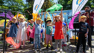 Kinder der Ev. Kita Gadeland aus Neumünster singen zusammen mit Lukas Johannsen "LiederLukas" (ganz rechts) den Jubiläumssong "Mehr von Morgen"
