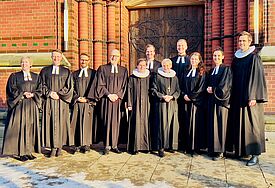 Ordiantionsgottesdienst: Zehn Pastorinnen und Pastoren und Bischöfin Kirsten Fehrs stehen im Talar vor einer Kirche.