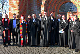 Gruppe an Menschen in Talaren steht vor der Kirche