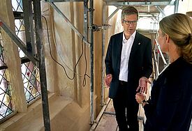 Die beiden Personen stehen neben dem verzierten Fenster, durch das Licht in die Kirche dringt