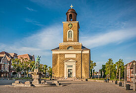 Die Sonne scheint auf die Marienkirche in Husum, die inmitten des Marktplatzes steht. Der Himmel ist blau mit einem sanften Wolkenschleier.
