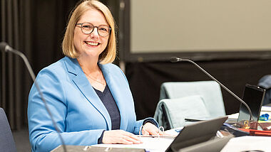 Präses Anja Fährmann sitzt am Laptop und lächelt in. die Kamera.
