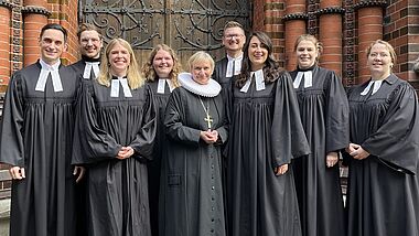 Die neuen Pastorinnen und Pastoren stehen vor der Kirchentür von St. Gertrud. In ihrer Mitte Bischöfin Kirsten Fehrs im Ornat und mit Amtskreuz.