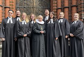 Die neuen Pastorinnen und Pastoren stehen vor der Kirchentür von St. Gertrud. In ihrer Mitte Bischöfin Kirsten Fehrs im Ornat und mit Amtskreuz.