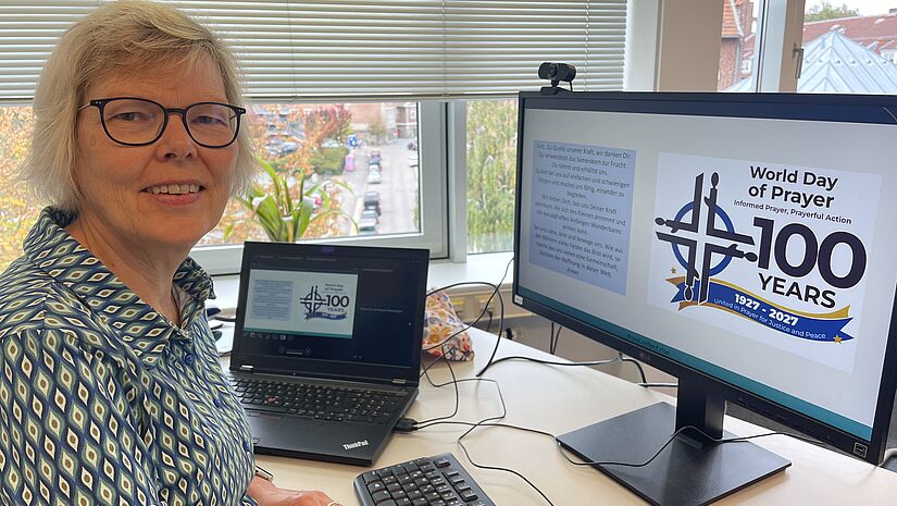 Frau am Schreibitsch, auf dem Monitor ist 100 Years World Day of Prayer" zu lesen.