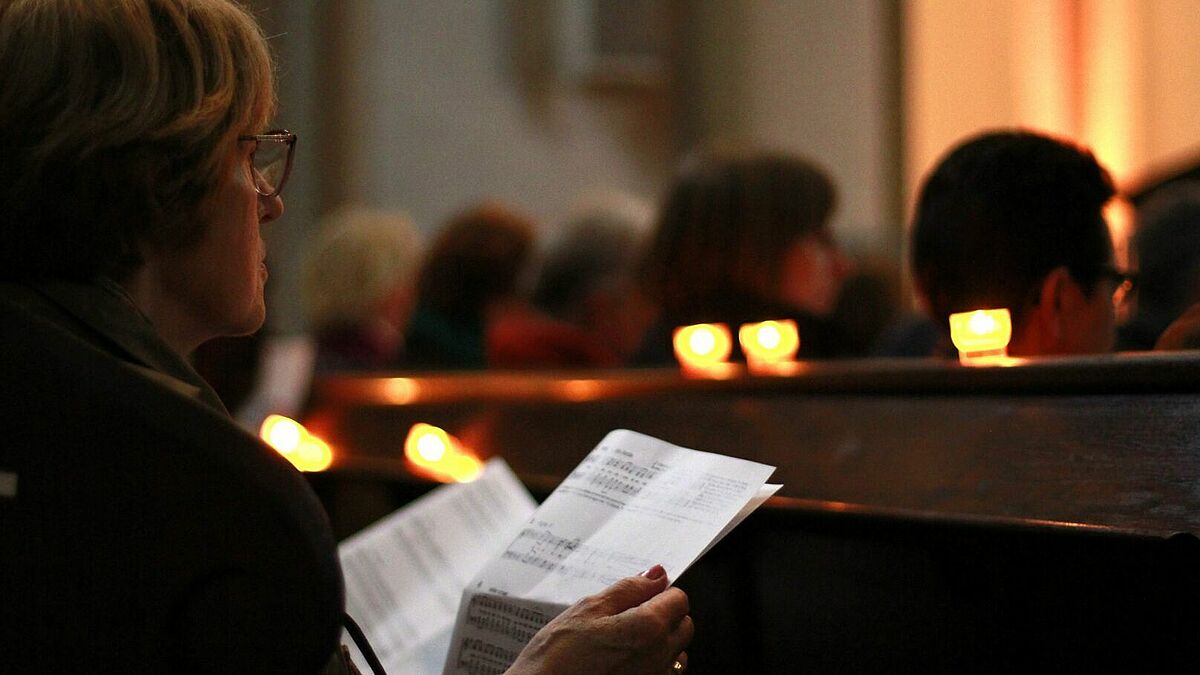 Eine Frau liest in der Hauptkirche St. Petri bei Kerzenschein den Liederzettel