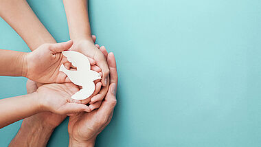 Adult and child hands holding white dove bird on blue background, international day of peace or world peace day concept, sustainable consumption, csr responsible business concept