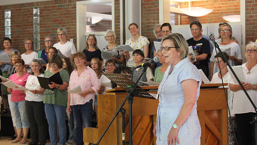 Ein Frau steht am Mikro und singt. Im Hintergrund steht ein Chor.