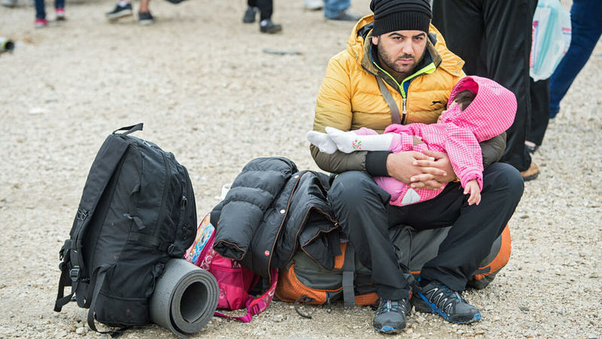 Ein Flüchtling sitzt mit einem Kleinkind auf seinem Rucksack in der Pufferzone im griechischen Idomeni an den Gleisen und wartet auf den Grenzübertritt.