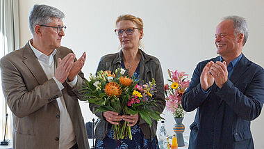 Pröpstin Carstensen mit Blumen. Neben ihr stehen Präses Heydemann und Bischof Jeremias.
