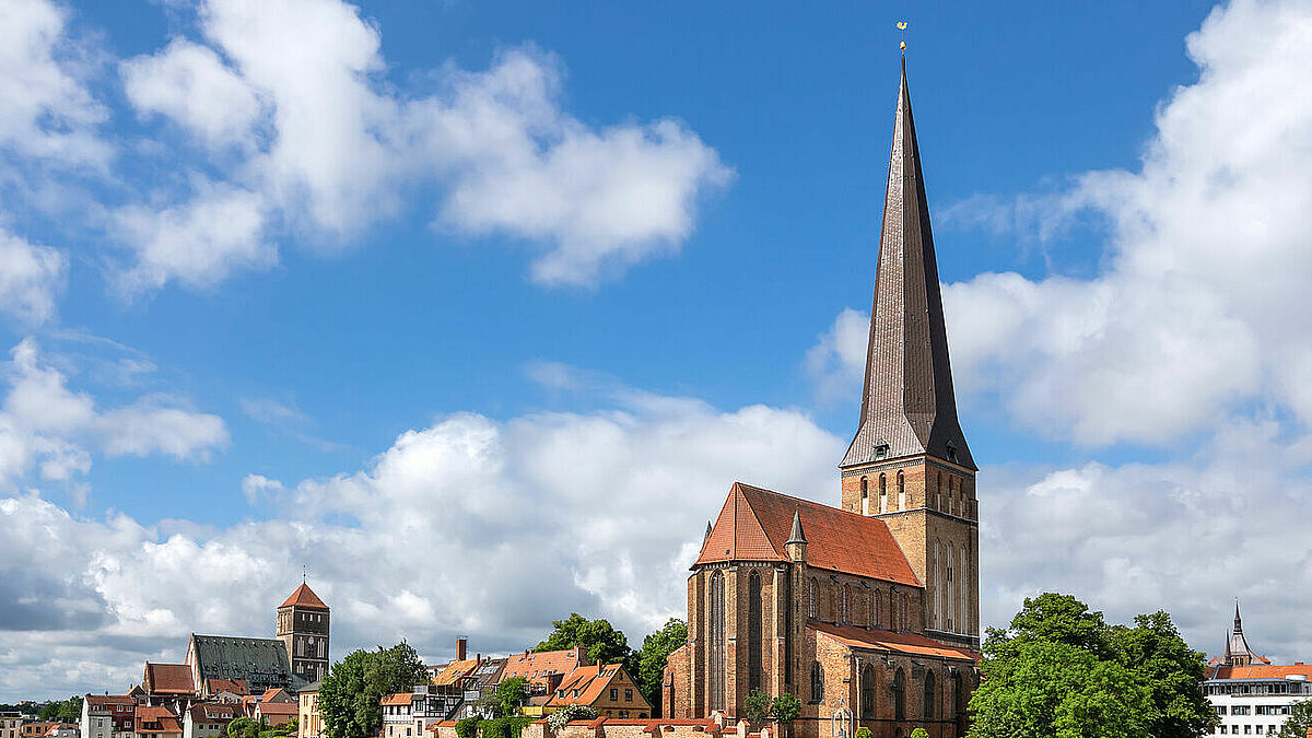 Die Petrikirche (rechts) ist die älteste und mit ihren 117 Metern auch die höchste der ehemals vier Stadtkirchen Rostocks. Von einer Aussichtsplattform können Besucher den Blick über die Hansestadt genießen. Im Hintergrund zu sehen: die Nikolaikirche.