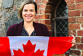 Caroline Raddatz lächelt und hält die rot-weiße kanadische Flagge mit einem Ahornblatt