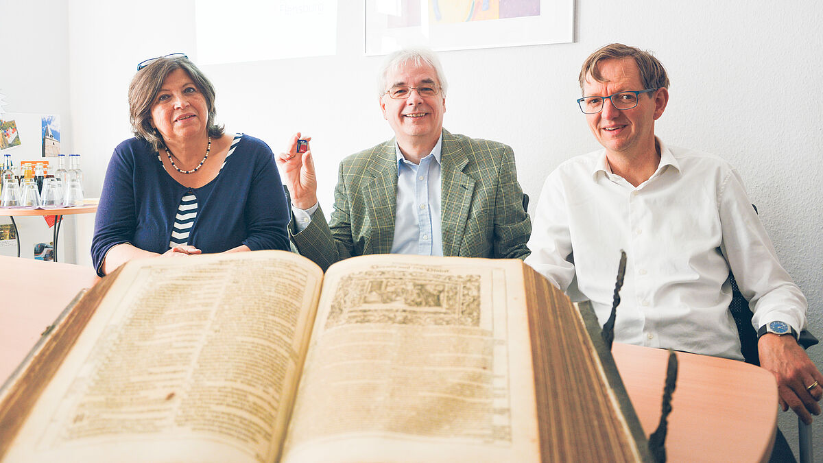 Von einer alten Schrift bis hin zum Mikrochip: Pröpstin Carmen Rahlf (v.l.), Dr. Heinz Peter Mauelshagen und Wolfgang Schmutz präsentieren eine Bibelausstellung in Flensburg.