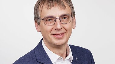 Porträtfoto von einem Mann mit Anzug und Brille.