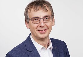 Porträtfoto von einem Mann mit Anzug und Brille.