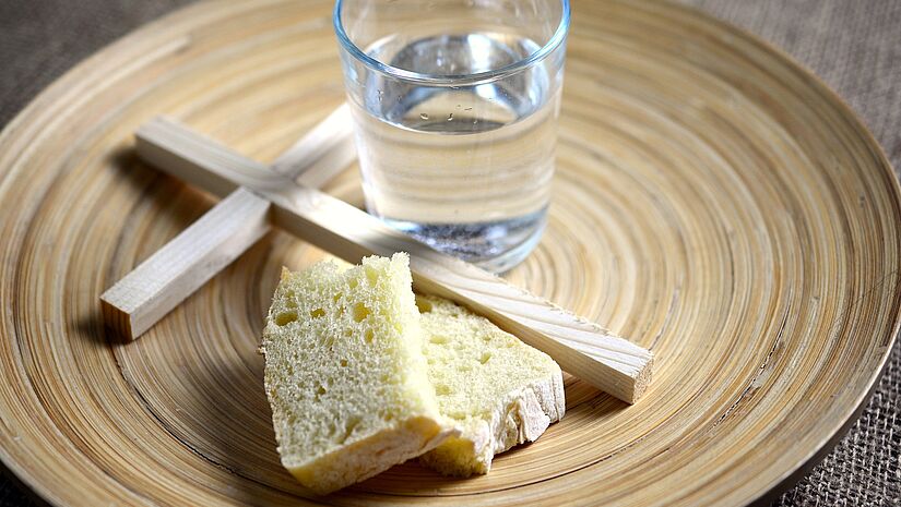 Teller mit Brot, Wasser und Holzkreuz