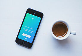 Kaffee neben einem Smartphone, auf dem Twitter geöffnet ist