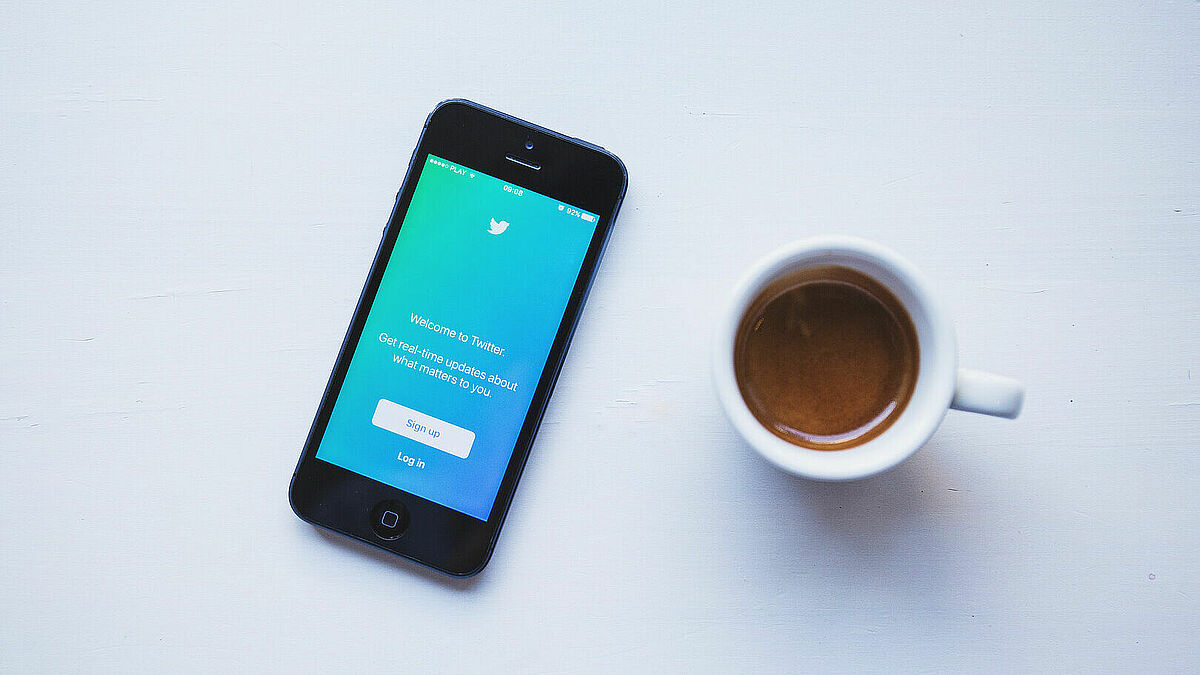 Kaffee neben einem Smartphone, auf dem Twitter geöffnet ist