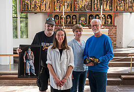 Hempels-Verkäufer Jan zeigt sein "Goldgräber-Bild" in der Nikolai-Kirche Kiel, in der es ausgestellt wird. Mit dabei sind Mitglieder des Hempels-Teams sowie der Fotograf Holger Förster. 