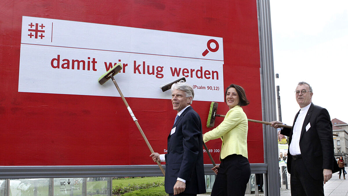 "Damit wir klug werden" – Generalsekretärin Ellen Ueberschär plakatiert das Motto des Kirchentags, unterstützt von Kirchentagspräsident Andreas Barner (l.) und dem württembergischen Landesbischof Otfried July