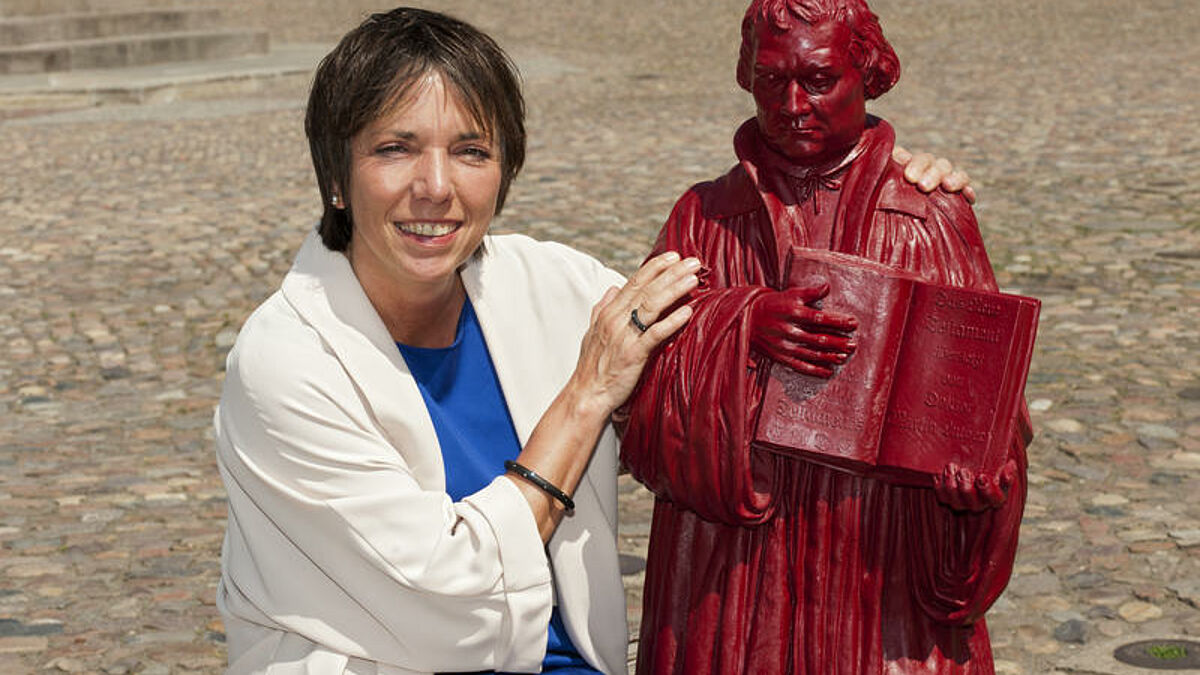 Die neue Reformations-Botschafterin der Evangelischen Kirche in Deutschland (EKD), Margot Käßmann, am 22.05.2012 mit einer roten Luther-Skulptur des Künstlers Ottmar Hörl auf dem Marktplatz in Wittenberg. Die Kunststoffplastik ist eine Miniaturkopie des Lutherdenkmals auf dem Wittenberger Marktplatz. Käßmann trägt einen Armreif und einen Ring des Schmuckdesigners André Ribeiro. Die frühere EKD-Ratsvorsitzende Käßmann hatte Ende April ihr neues Botschafter-Amt übernommen. Die 2008 eröffnete Themenreihe soll bundesweit mit verschiedensten Veranstaltungen bis 2017 führen. Dann jährt sich der legendäre Thesenanschlag Martin Luthers (1483-1546) an der Wittenberger Schlosskirche zum 500. Mal. Das Ereignis gilt als Beginn der Kirchenreformation.