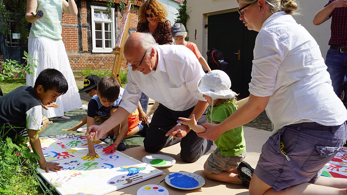 „Tag des Miteinanders“ im Parchimer Haus der Begegnung „M41“ der Kirchengemeinden Parchim St. Marien und Damm am 23. Mai 2017: Gemeinsam mit Kindern einheimischer und geflüchteter Familien malt Landesbischof Ulrich ein Wandbild zum Thema „Frieden“. Das aus mehreren Leinwänden bestehende Gemeinschaftswerk soll künftig die Räume des „M41“ schmücken. Foto: Döbler/Nordkirche