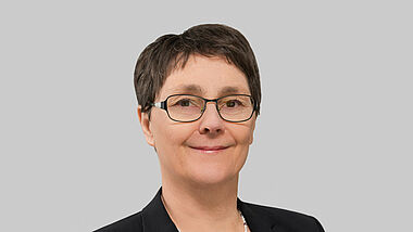 Porträt von Monika Heinold. Die Finanzministerin trägt einen schwarzen Blazer über einem blau-weiß-gestreiften Shirt.
