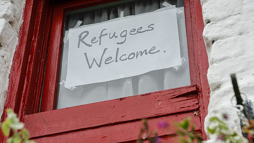 Schild in einem Roten Fenster mit Aufschrift "Refugees welcome"