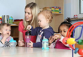 Eine junge Frau sitzt mit Kindern am Tisch, die aus Trinkfalschen trinken