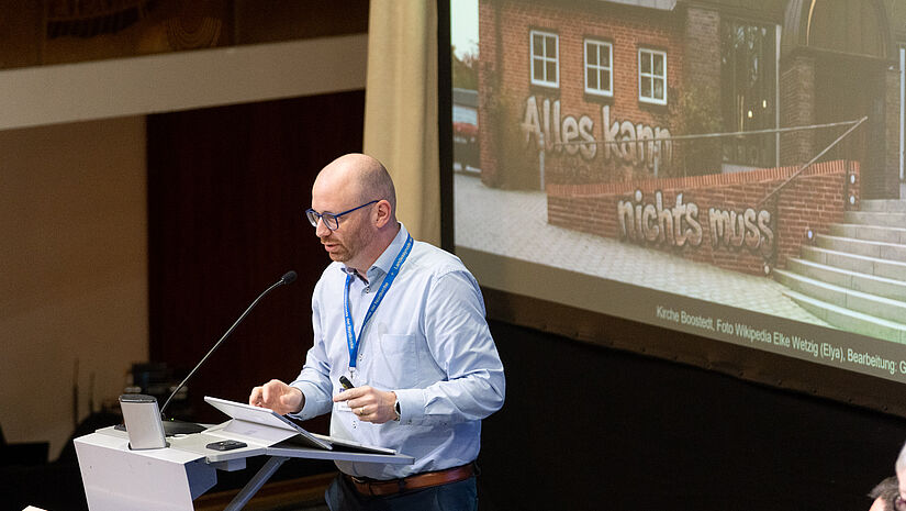 Ein Mann steht am Rednerpult und spricht in ein Mikro. 