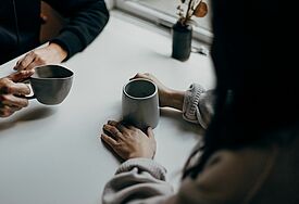 Kaffeebecher und zwei Paar Hände 