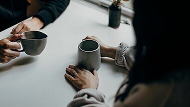 Kaffeebecher und zwei Paar Hände 