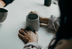 Kaffeebecher und zwei Paar Hände 