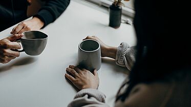 Kaffeebecher und zwei Paar Hände 