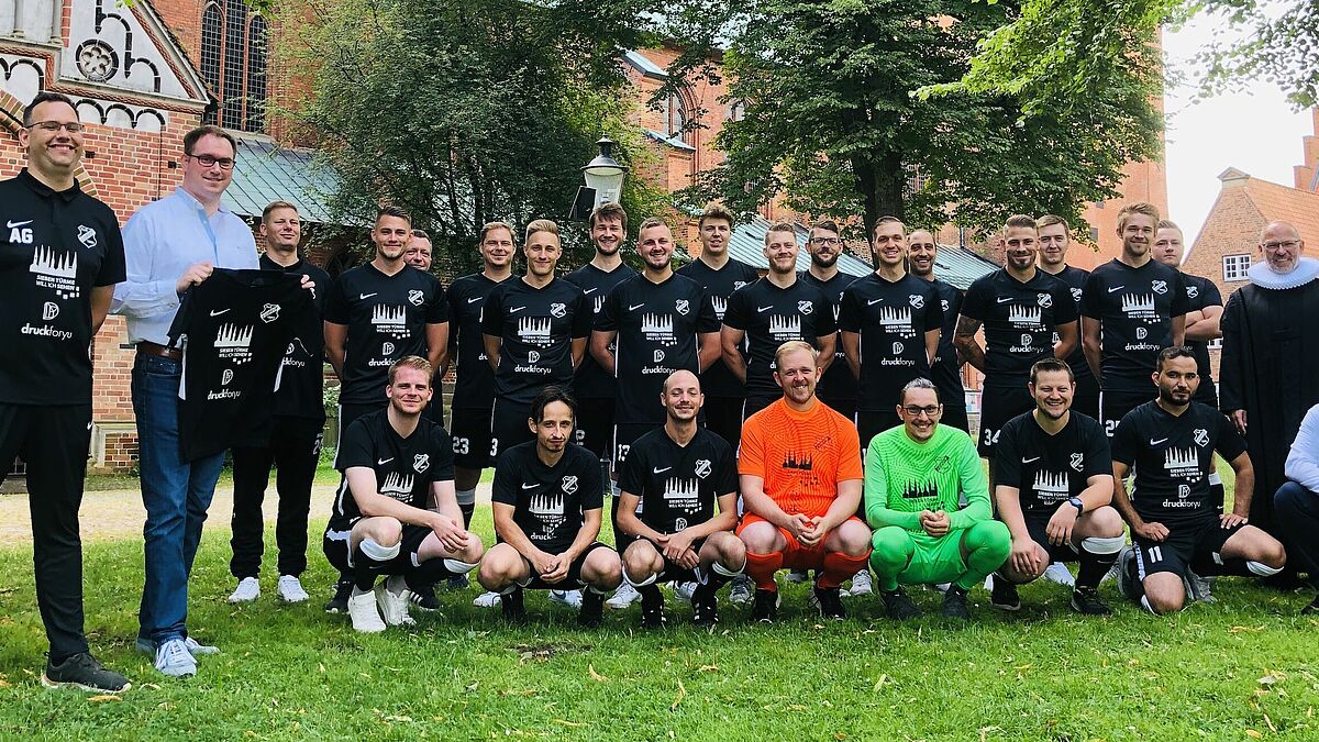 Trainer André Guhlke, Bürgermeister Jan LIndenau (1. Und 2. V. li.) sowie Dennis Forte, Inhaber von druckfory (re, hockend) und Pastor Martin Klatt präsentieren die neuen T-Shirts der mit den Spielern der 2. Herrenmannschaft des TuS Lübeck von 1893 e. V..